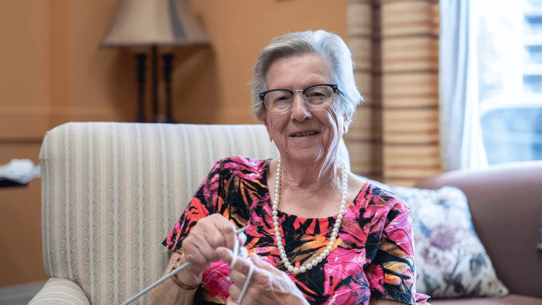 An elderly woman knitting while sitting on sofa